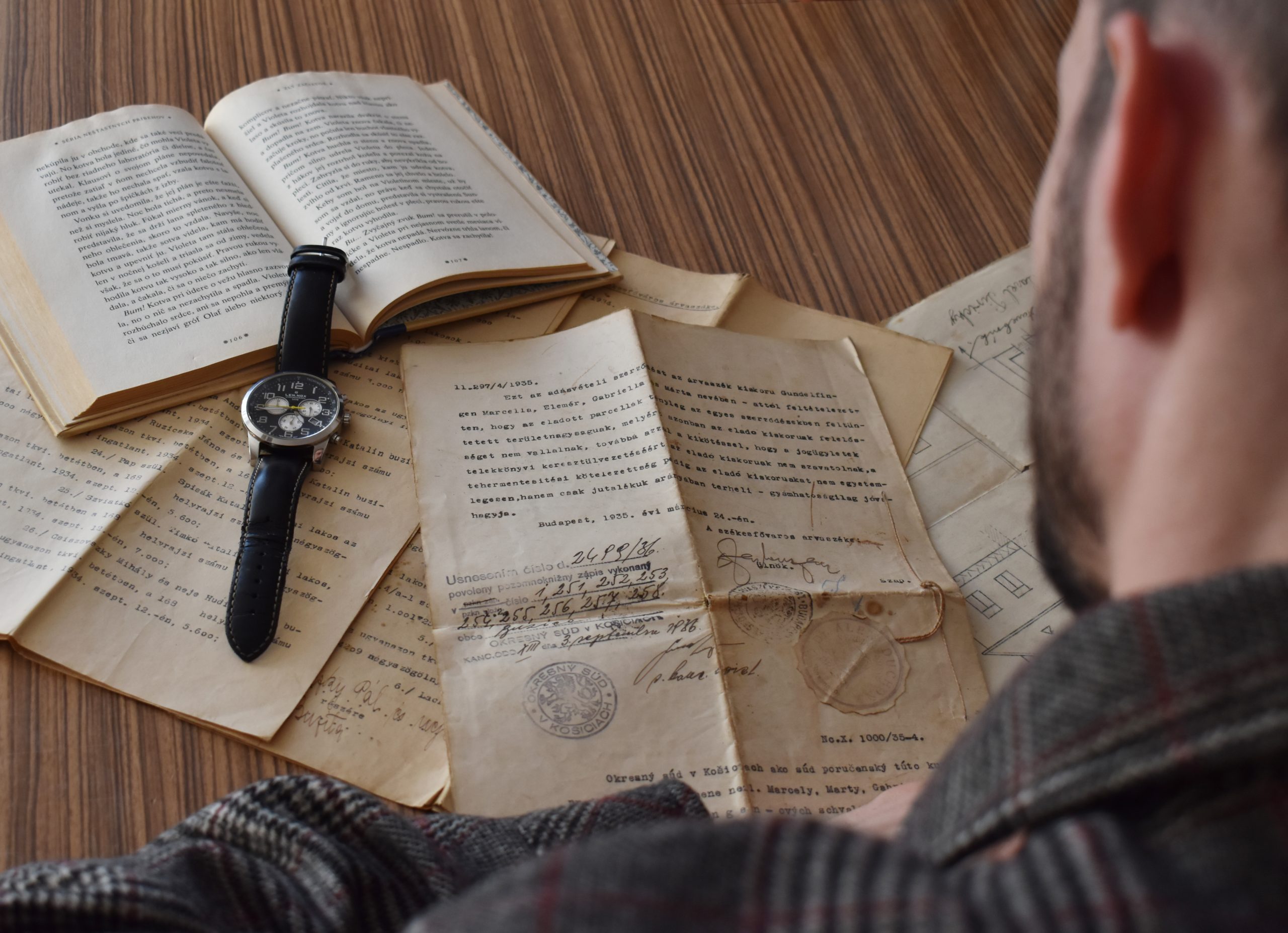 muž číta staré dokumenty s hodinkami na knihe